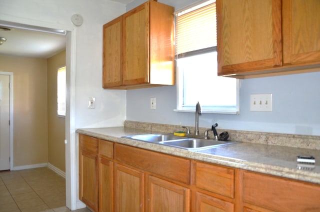 kitchen with brown cabinets, light countertops, a sink, light tile patterned flooring, and baseboards