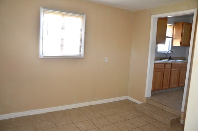 spare room with light tile patterned flooring, a healthy amount of sunlight, baseboards, and a sink