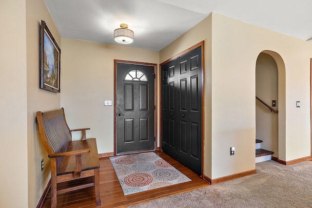 foyer with wood finished floors, baseboards, arched walkways, and stairs