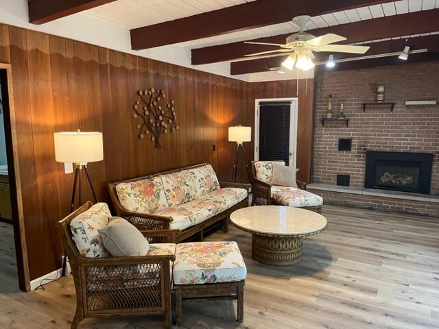 608 Terrace Dr, Houghton Lake, MI 48629 - living room featuring beamed ceiling, a ceiling fan, wood finished floors, a brick fireplace, and wooden walls