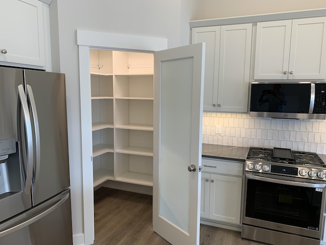 12580 Riverton Rd, Grand Haven, MI 49417 - kitchen featuring stainless steel appliances, dark wood-style floors, tasteful backsplash, and dark countertops