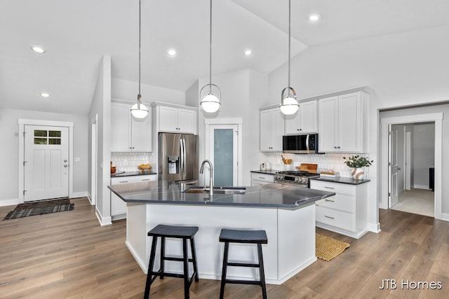 12580 Riverton Rd, Grand Haven, MI 49417 - kitchen featuring appliances with stainless steel finishes, dark countertops, vaulted ceiling, a kitchen island with sink, and decorative backsplash