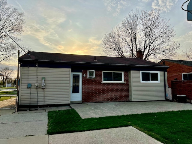 back of property at dusk with brick siding, a patio area, a chimney, and fence