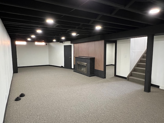 basement featuring baseboards, carpet flooring, a glass covered fireplace, and stairway