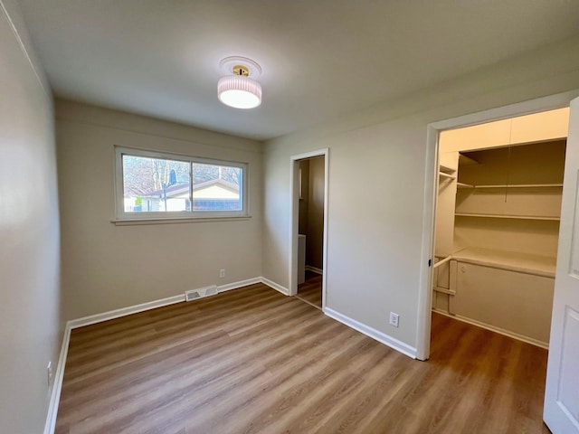 unfurnished bedroom with a spacious closet, baseboards, wood finished floors, and visible vents