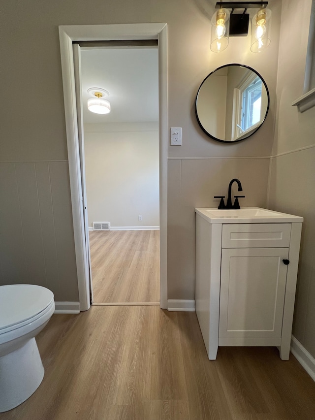 half bathroom featuring wood finished floors, visible vents, toilet, and vanity