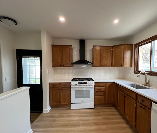kitchen featuring brown cabinetry, wall chimney range hood, a sink, and white gas range oven