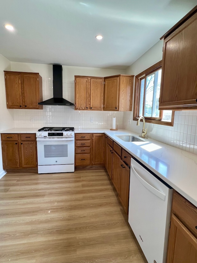 kitchen with wall chimney range hood, brown cabinets, a sink, and white appliances