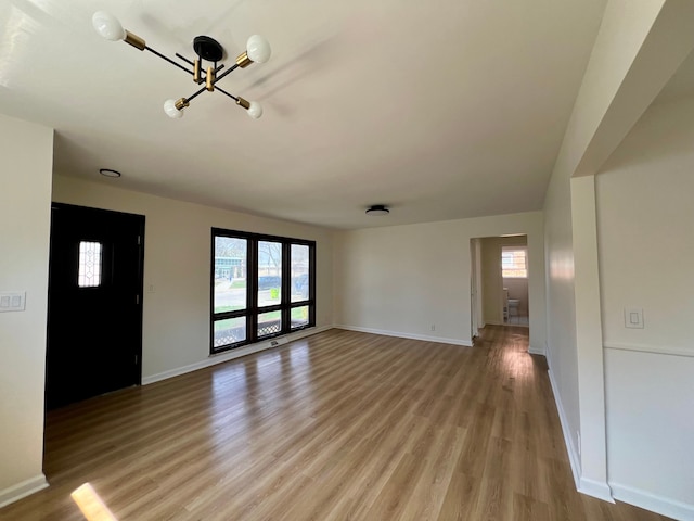 unfurnished living room with baseboards, a chandelier, and light wood finished floors