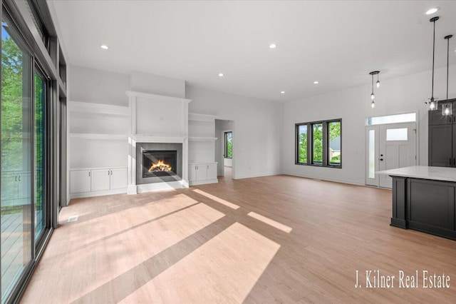 9465 Wabasis Pointe Dr NE, Greenville, MI 48838 - unfurnished living room with light wood-style flooring, a lit fireplace, recessed lighting, and baseboards