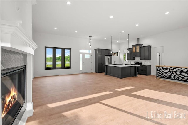 9465 Wabasis Pointe Dr NE, Greenville, MI 48838 - kitchen featuring a glass covered fireplace, a center island with sink, open floor plan, stainless steel refrigerator, and light countertops