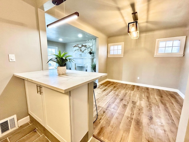 10342 Britain St, Detroit, MI 48224 - kitchen with a kitchen bar, visible vents, light stone counters, baseboards, and wood finished floors