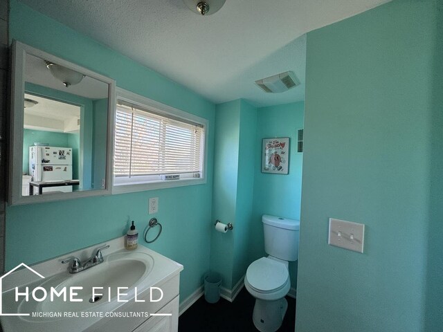 half bath featuring toilet, vanity, visible vents, and baseboards