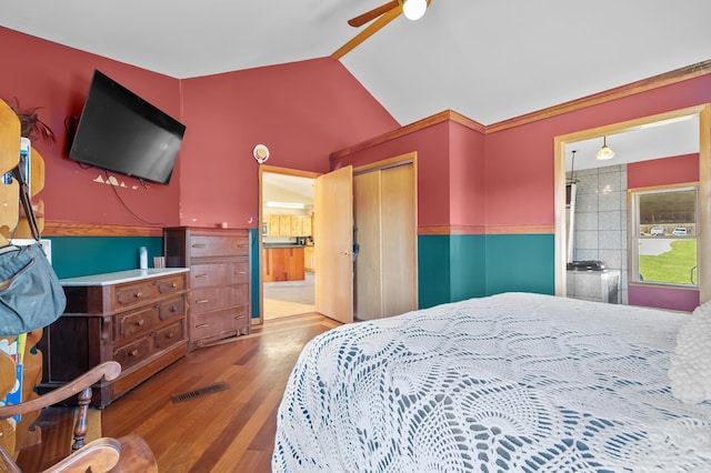 bedroom with vaulted ceiling, visible vents, wood finished floors, ensuite bath, and a closet