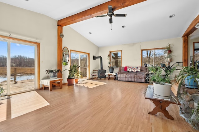 living area featuring a ceiling fan, wood finished floors, lofted ceiling with beams, a water view, and a wood stove