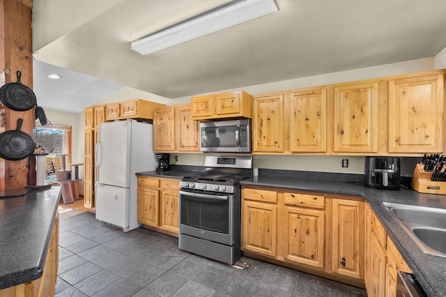 kitchen featuring recessed lighting, stainless steel appliances, dark countertops, light brown cabinets, and a sink