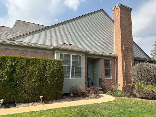 5081 Belmonte Dr, Rochester, MI 48306 - view of side of property with a shingled roof, a chimney, brick siding, and a yard