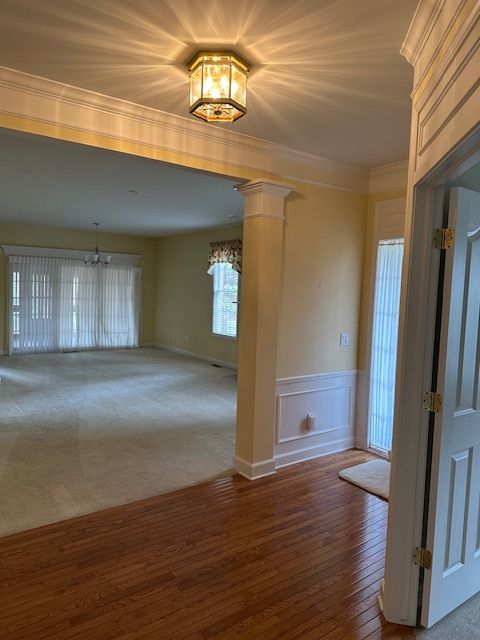 5081 Belmonte Dr, Rochester, MI 48306 - empty room featuring decorative columns, wood-type flooring, crown molding, wainscoting, and a chandelier