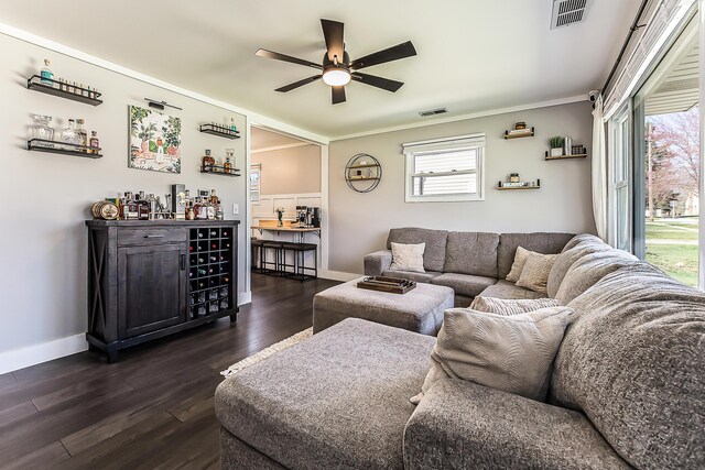 living area featuring dark wood-style floors, baseboards, visible vents, a ceiling fan, and crown molding