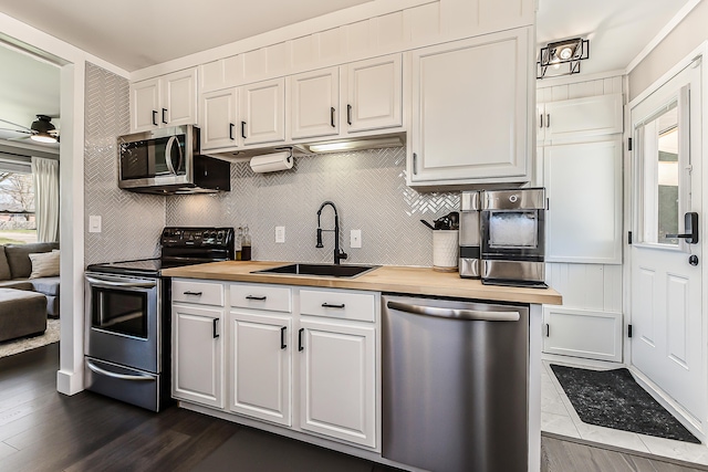 kitchen featuring stainless steel appliances, a ceiling fan, a sink, tasteful backsplash, and white cabinetry