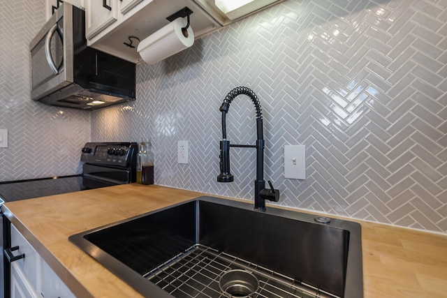 kitchen featuring white cabinets, a sink, stainless steel microwave, black electric range, and butcher block counters