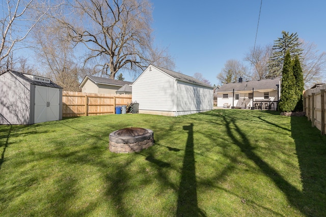view of yard featuring a fire pit, a storage unit, a fenced backyard, and an outdoor structure