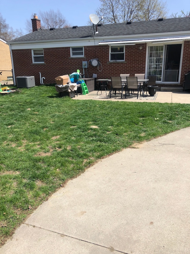 back of property with a chimney, brick siding, a patio area, and a yard