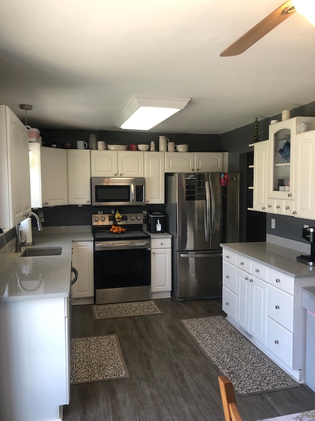 kitchen with a ceiling fan, a sink, appliances with stainless steel finishes, white cabinets, and dark wood-style flooring
