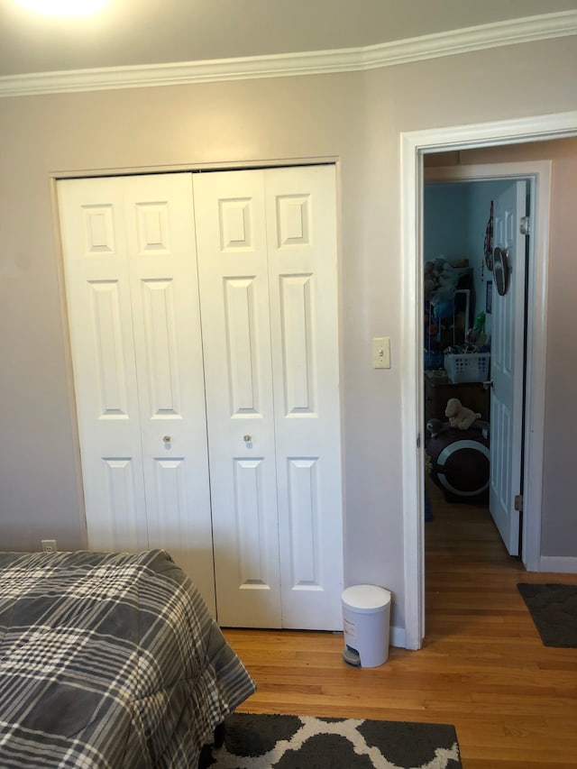 bedroom featuring light wood-style floors, a closet, crown molding, and baseboards