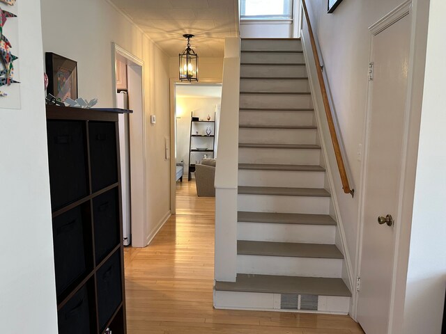 staircase with a notable chandelier, wood finished floors, and visible vents