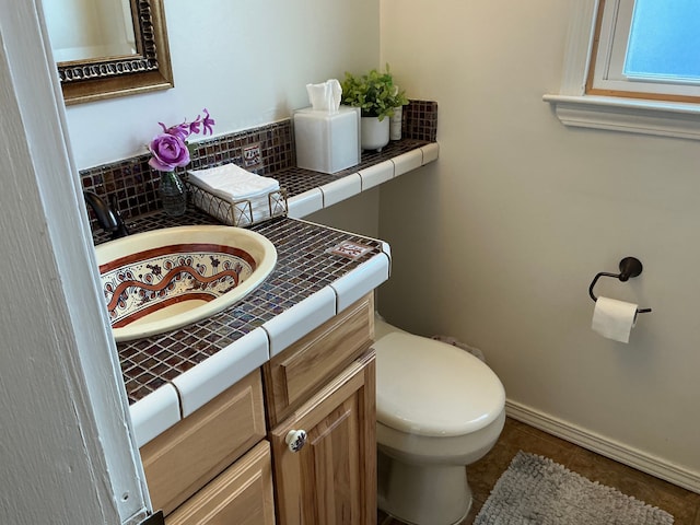 half bathroom with toilet, baseboards, decorative backsplash, tile patterned flooring, and vanity