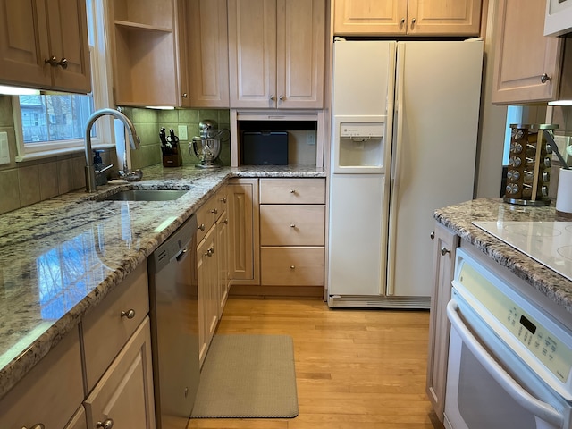 kitchen with light wood finished floors, light stone counters, a sink, white appliances, and decorative backsplash