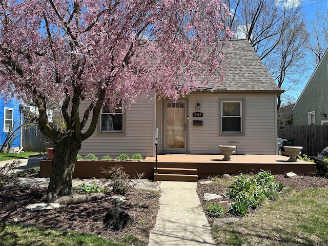 view of front of house featuring fence, a wooden deck, and roof with shingles