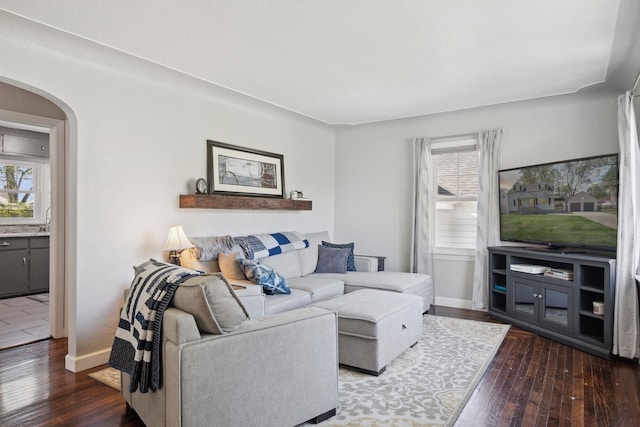 living room featuring arched walkways, plenty of natural light, baseboards, and hardwood / wood-style flooring