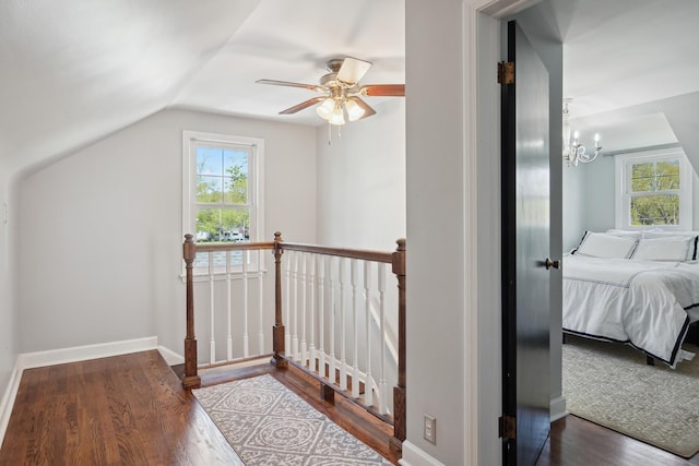 hall with wood finished floors, baseboards, a chandelier, vaulted ceiling, and an upstairs landing