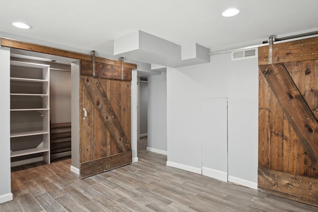 interior space with baseboards, wood finished floors, a barn door, and visible vents