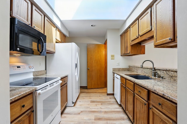 kitchen with light wood-style flooring, brown cabinetry, a sink, and white appliances