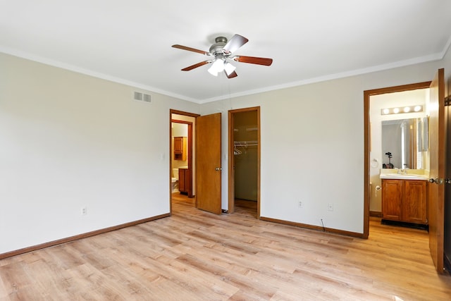 unfurnished bedroom featuring visible vents, baseboards, a spacious closet, light wood-style floors, and crown molding