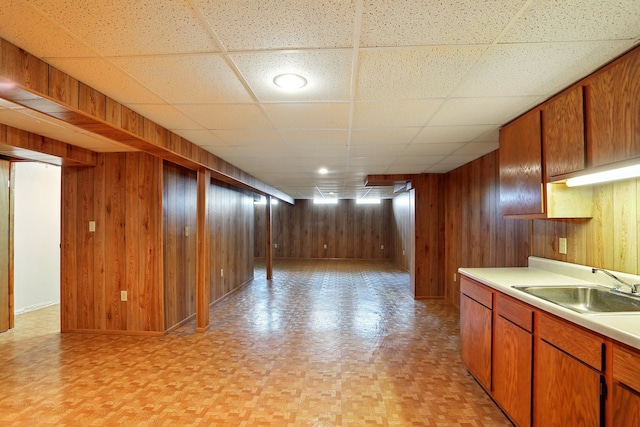 interior space with a paneled ceiling, wood walls, baseboards, and a sink
