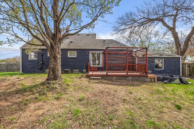 rear view of house featuring fence, a wooden deck, and a lawn