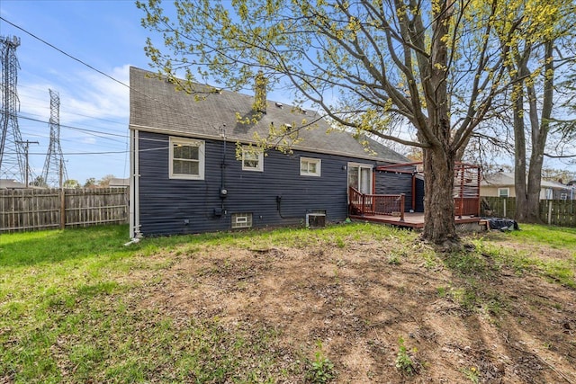 rear view of property featuring a deck, a fenced backyard, a shingled roof, central AC, and a lawn