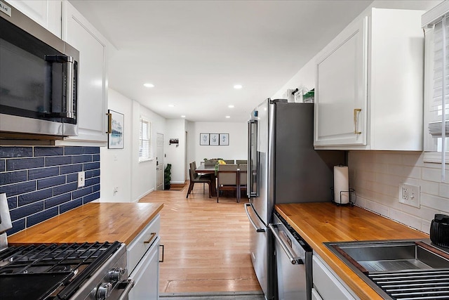 kitchen featuring wooden counters, white cabinets, backsplash, and stainless steel appliances