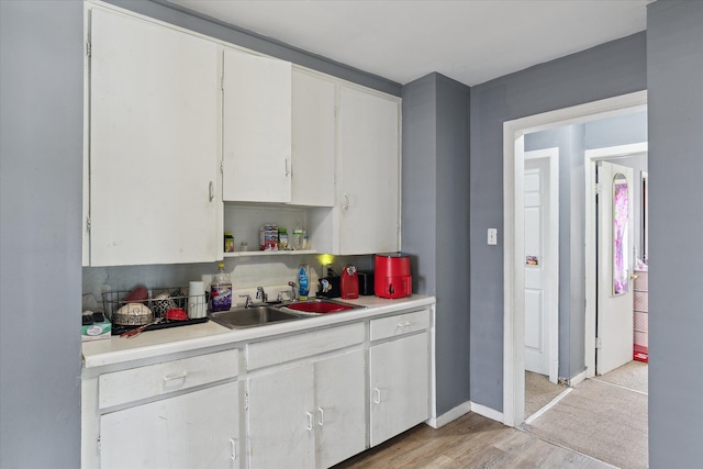 kitchen featuring a sink, light countertops, light wood-type flooring, white cabinets, and baseboards