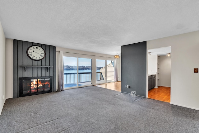 unfurnished living room featuring carpet floors, a textured ceiling, a large fireplace, and a water view