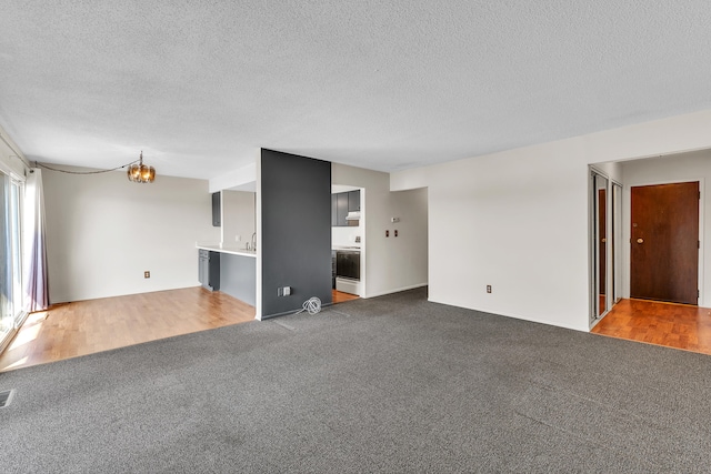 unfurnished living room with carpet flooring, a textured ceiling, and a notable chandelier