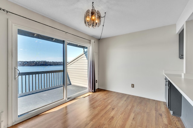 unfurnished dining area featuring a textured ceiling, a chandelier, a water view, and light wood-type flooring