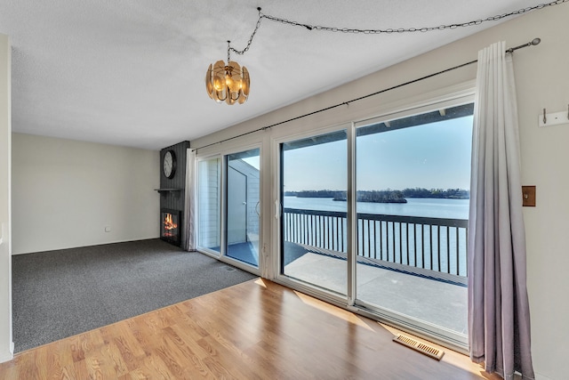 empty room with wood finished floors, a water view, an inviting chandelier, a large fireplace, and visible vents