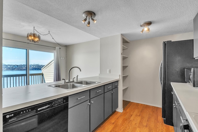 kitchen with light wood finished floors, a sink, a textured ceiling, light countertops, and black appliances
