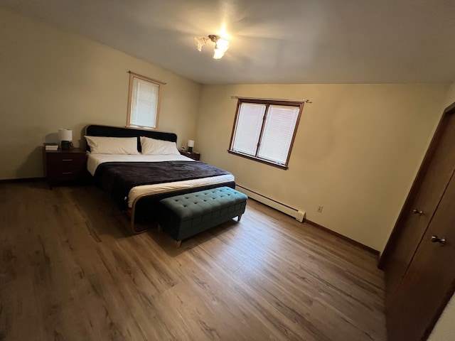 bedroom featuring a baseboard heating unit, baseboards, and wood finished floors