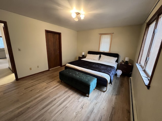 bedroom featuring a baseboard heating unit, wood finished floors, a closet, and baseboards